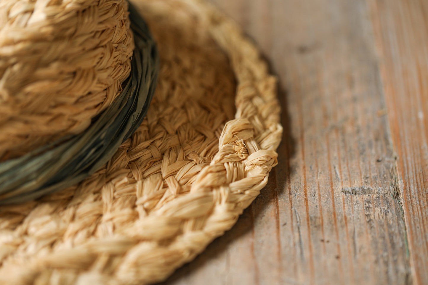 Close up shot of brim of handmade natural raffia hat placed on wooden surface. Hat has a green raffia twist decoration