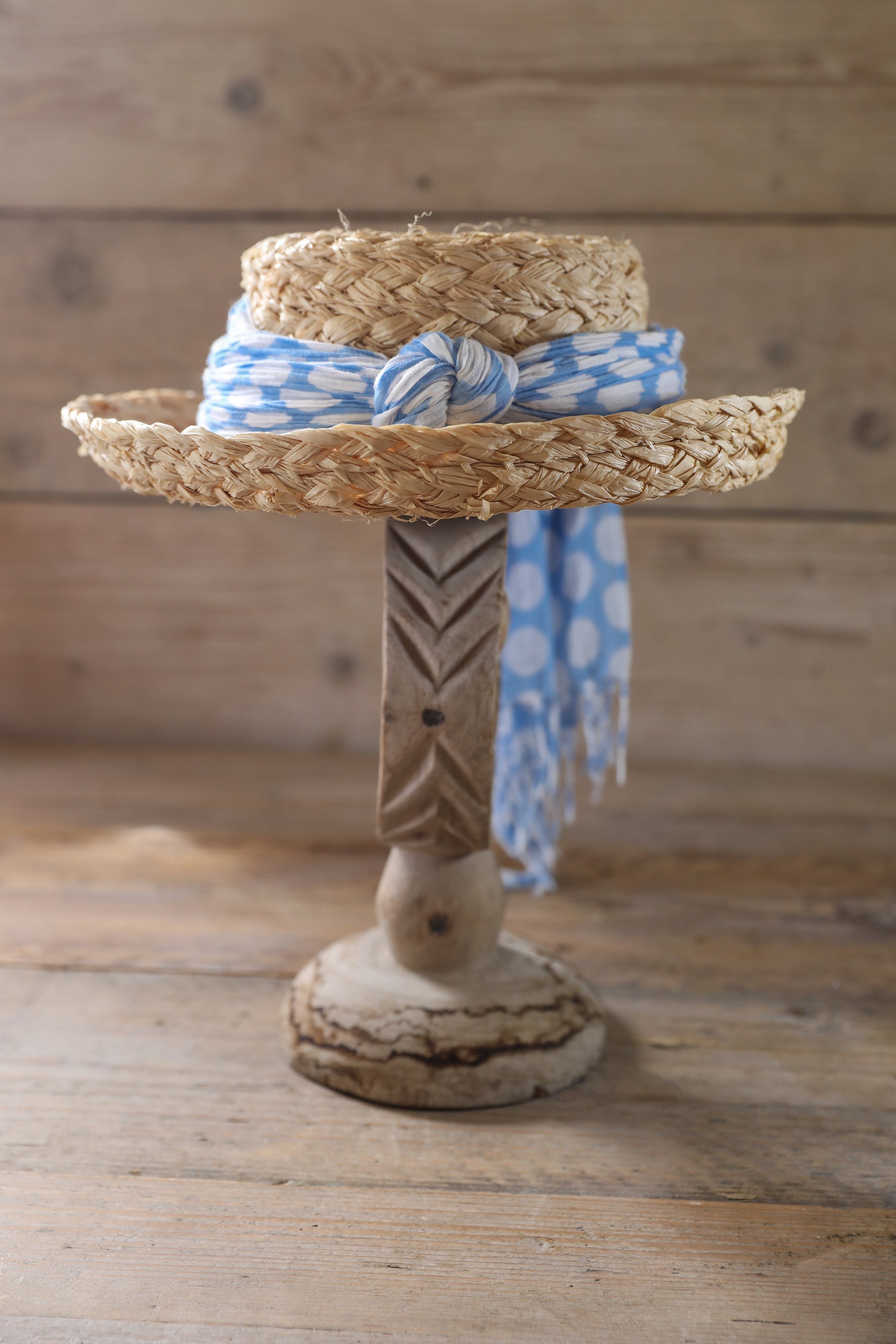 Decorative wooden stand with handmade natural raffia hat breton style on, featuring a blue and white fabric scarf finish.