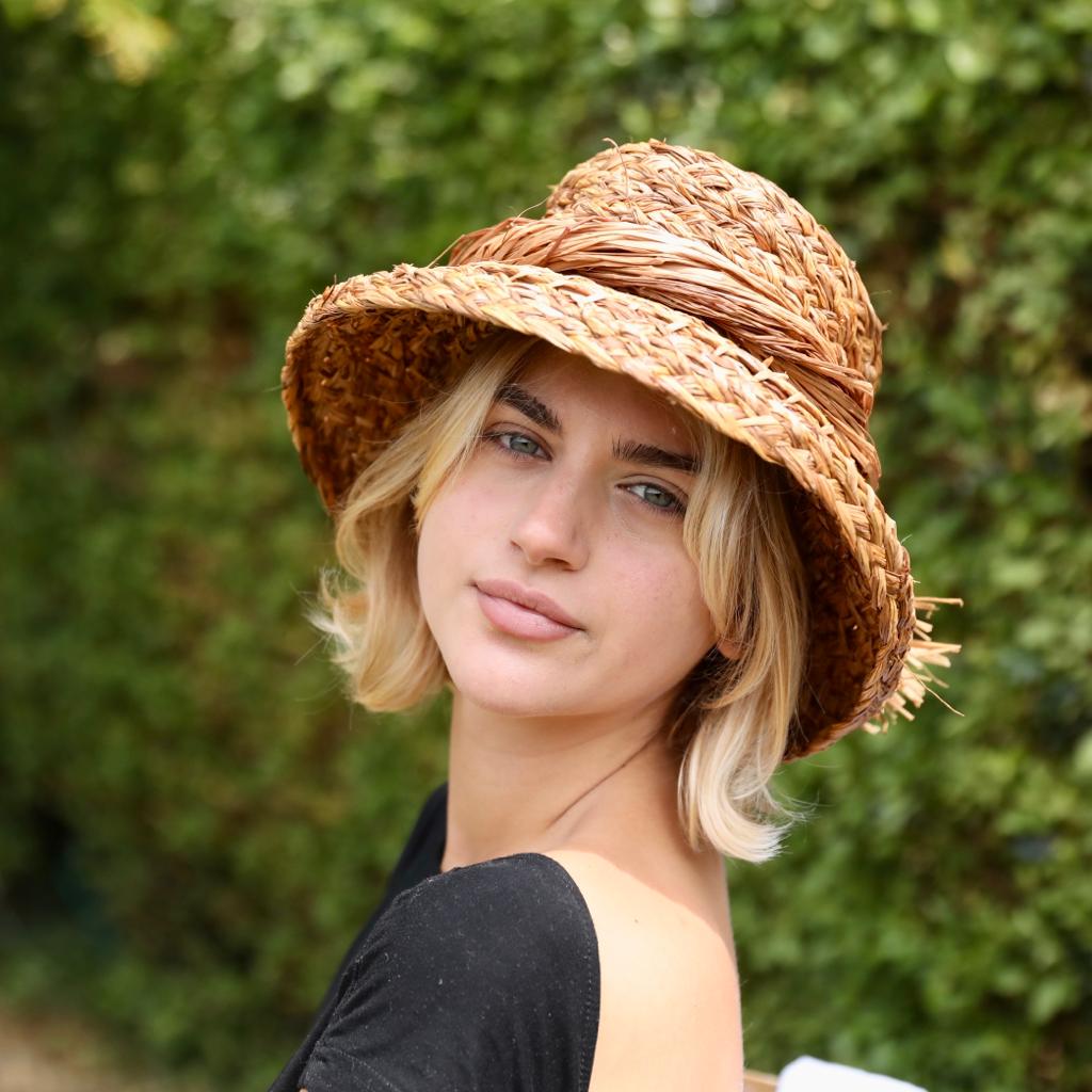 Woman wearing a handmade brown dyed raffia hat against a green background