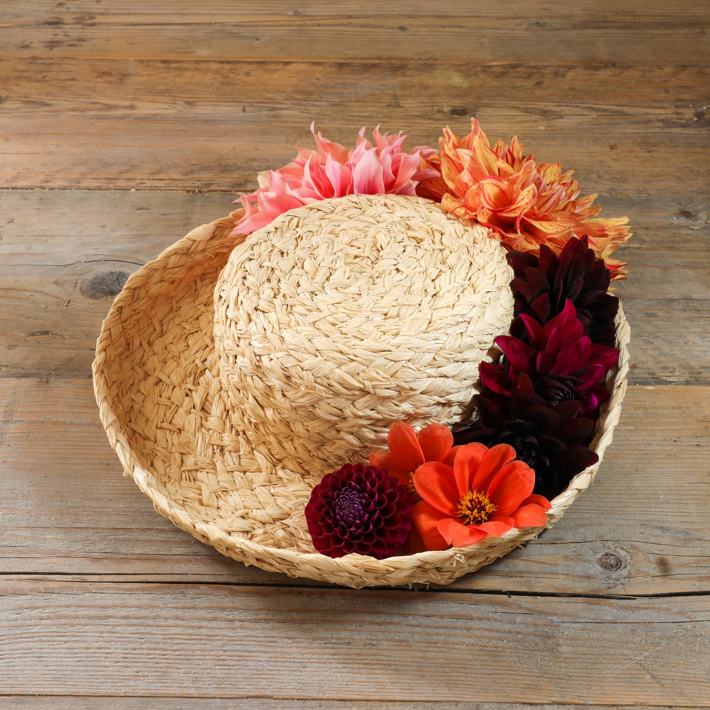 Natural handmade raffia hat with an upturned brim.  Hat on a wooden surface and fresh flowers placed in brim of hat.