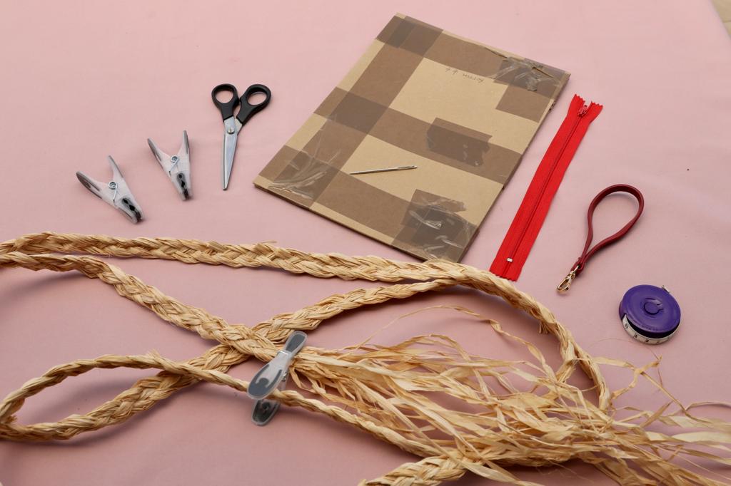 Equipment used in raffia craft to make a small clutch purse bag and a complete raffia course.  Scissors, pegs, needle, A4 card, zip, small handle plaited raffia, tape measure