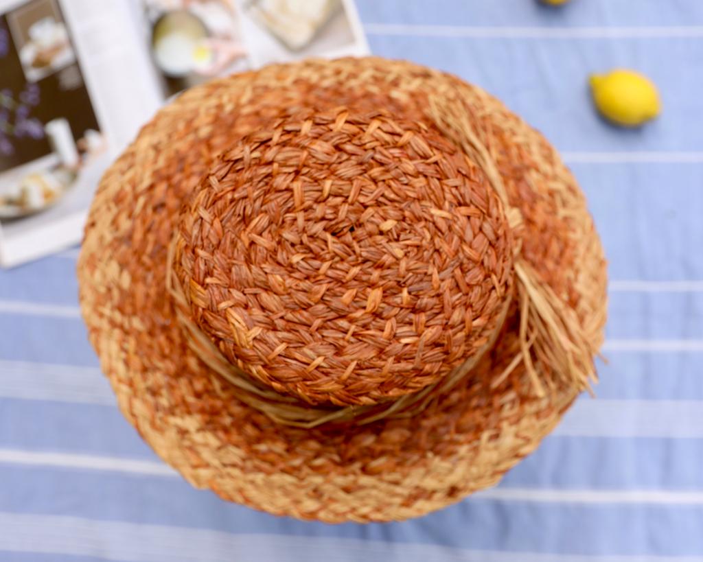 Plaited woven raffia hat which has been coloured using natural dyes.  Hat is placed on a blue striped surface