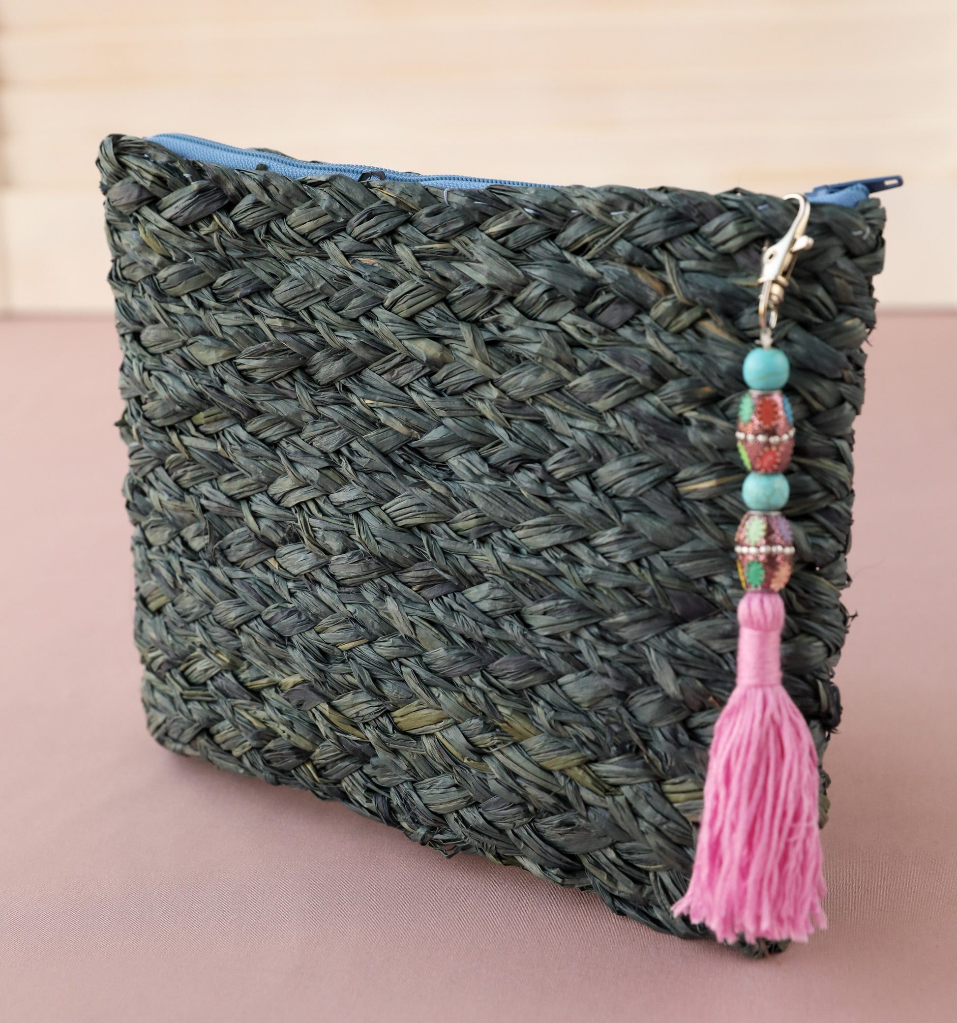 Handmade A5 size blue raffia clutch bag with blue zip and bead tassel decoration on pink background
