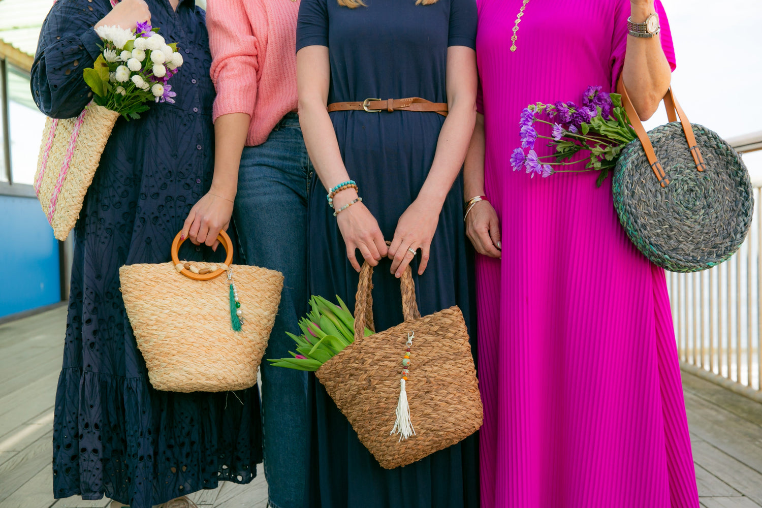 Four women holding handmade raffia bags with flowers on a UK seaside pier.