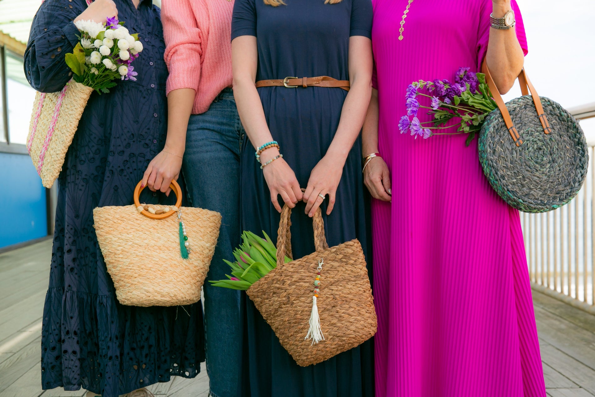 Four women holding handmade raffia bags with flowers on a UK seaside pier.