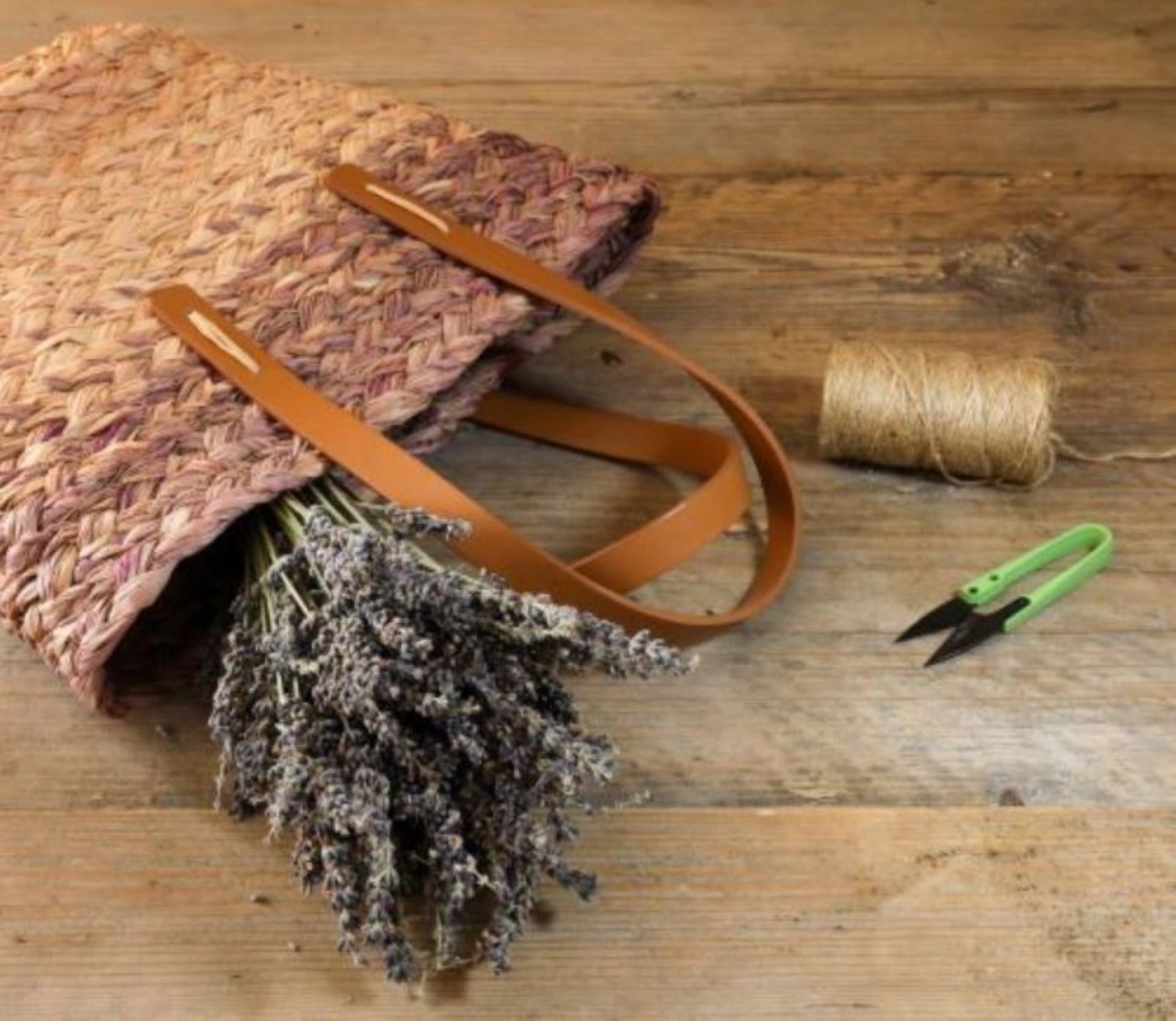 Raffia bucket bag with leather strap, on a wooden surface with lavender in it, twine and scissors nearby