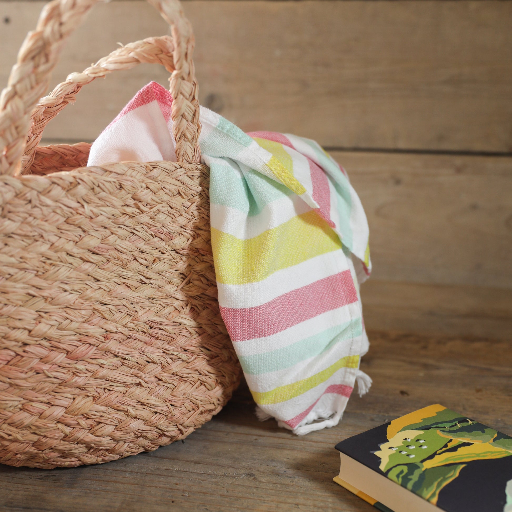 Raffia basket with a colorful striped towel on a wooden surface