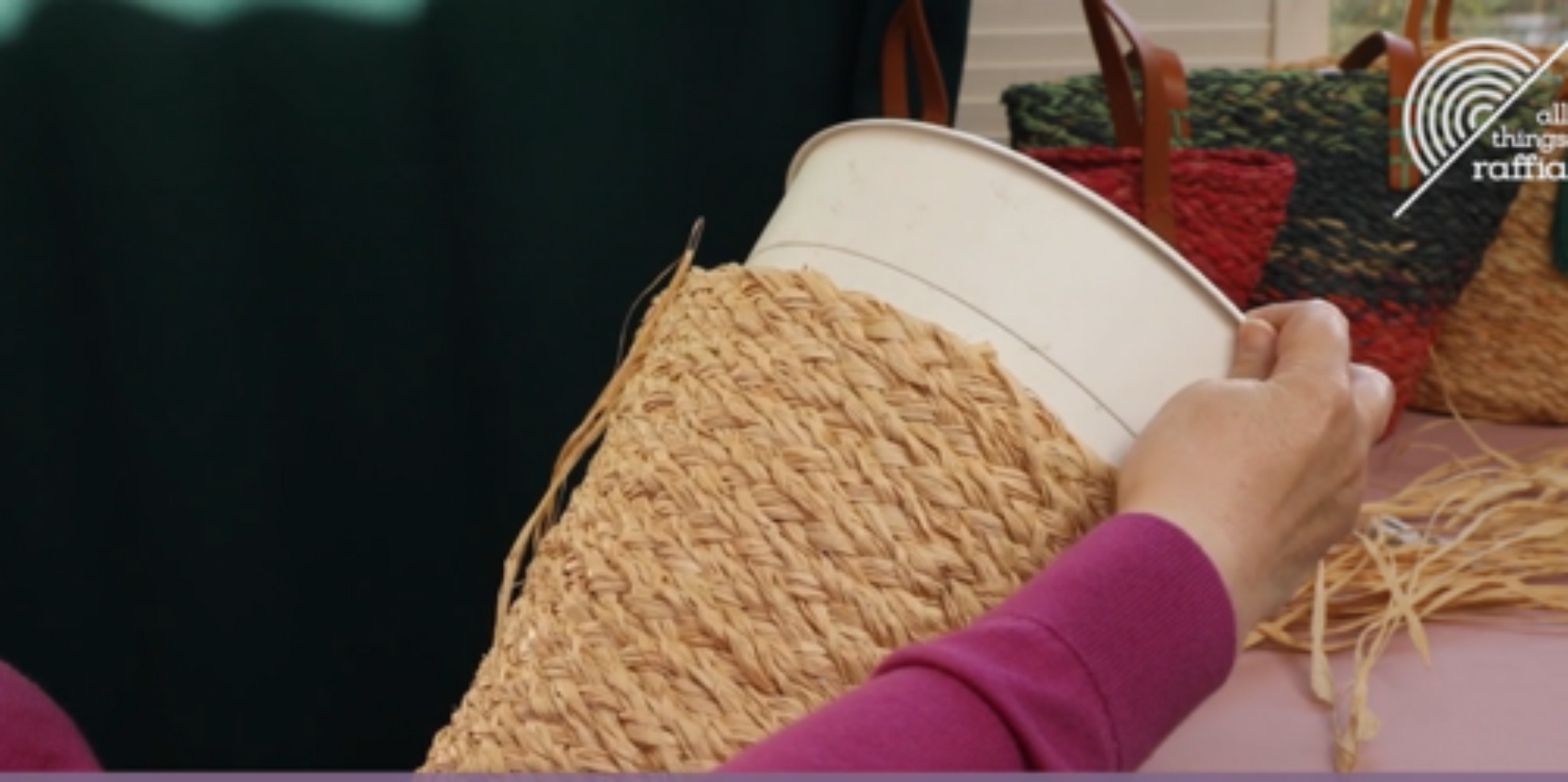 Screenshot from video of person working with raffia plait and sewing a bag on a bucket mold