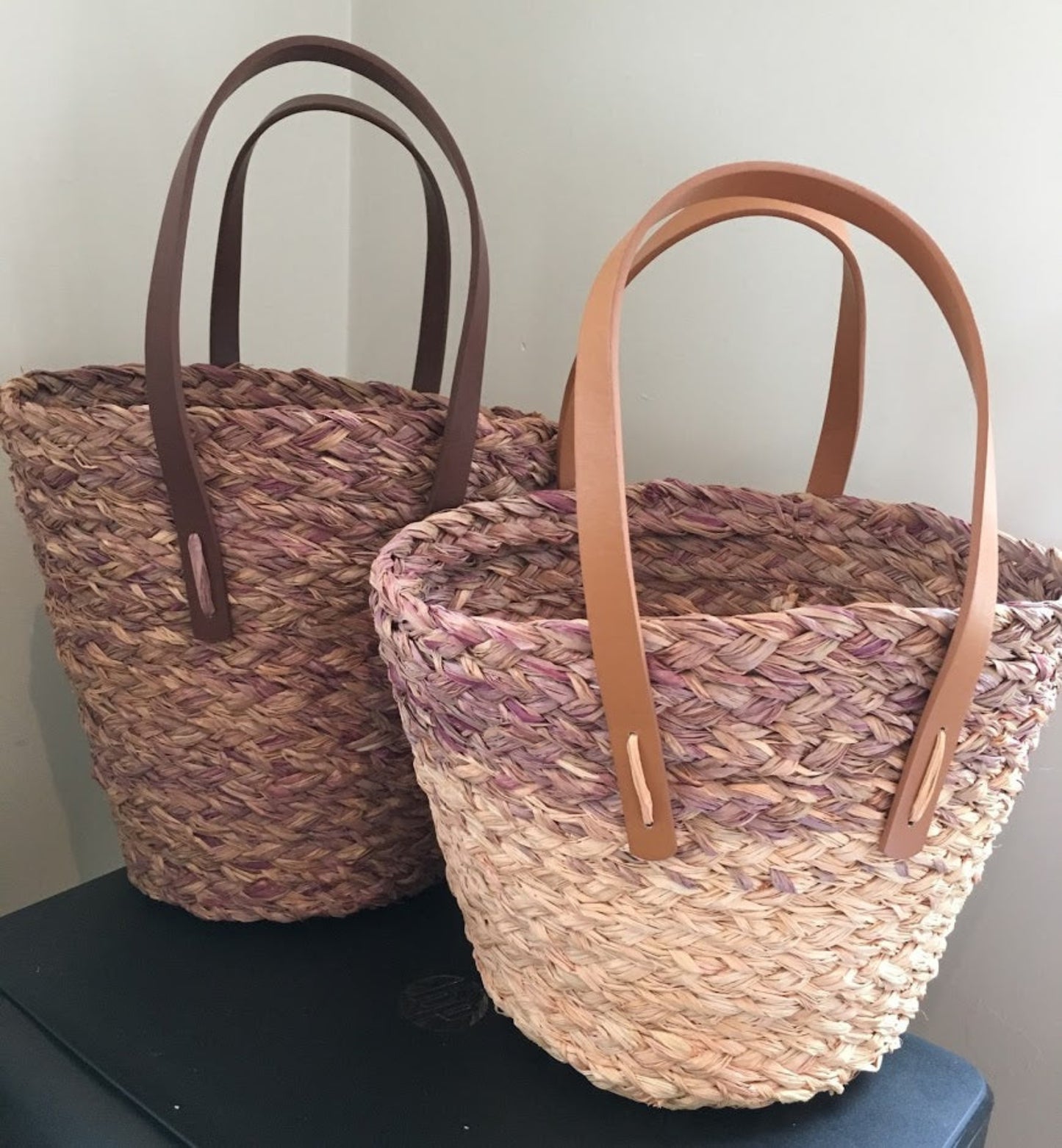 Two raffia bucket bags with shades of pink and leather-style handles